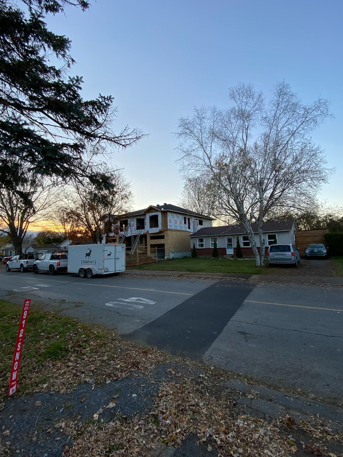 Construction site with a building frame, trees, and vehicles under a dusky sky.