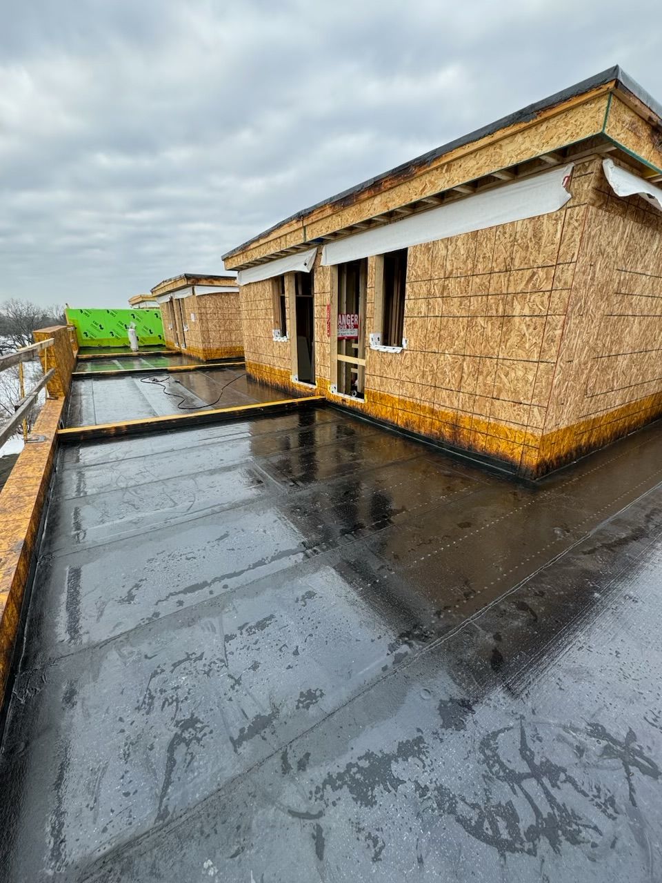 Construction site with flat roofs, exterior walls of wooden panels, overcast sky.