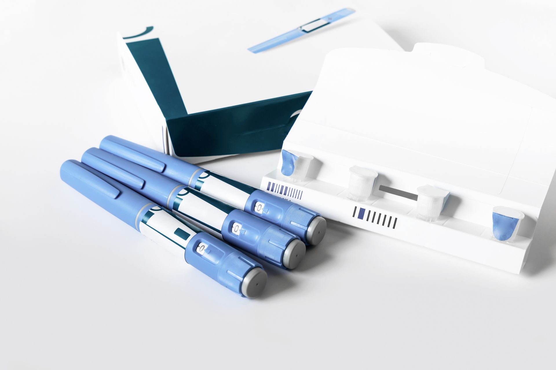 Four blue insulin pens and packaging on a white surface.