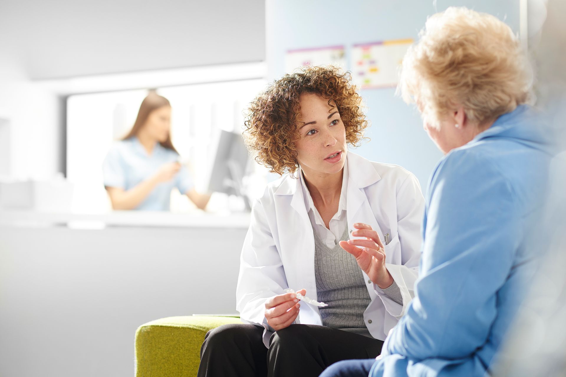 Doctor in white coat talking to patient, with nurse in background.