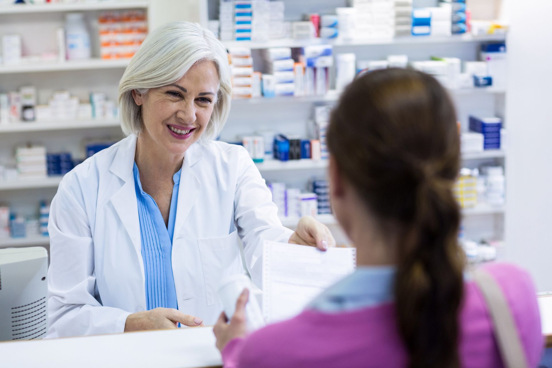 Pharmacist handing prescription bag to a customer at a pharmacy counter.