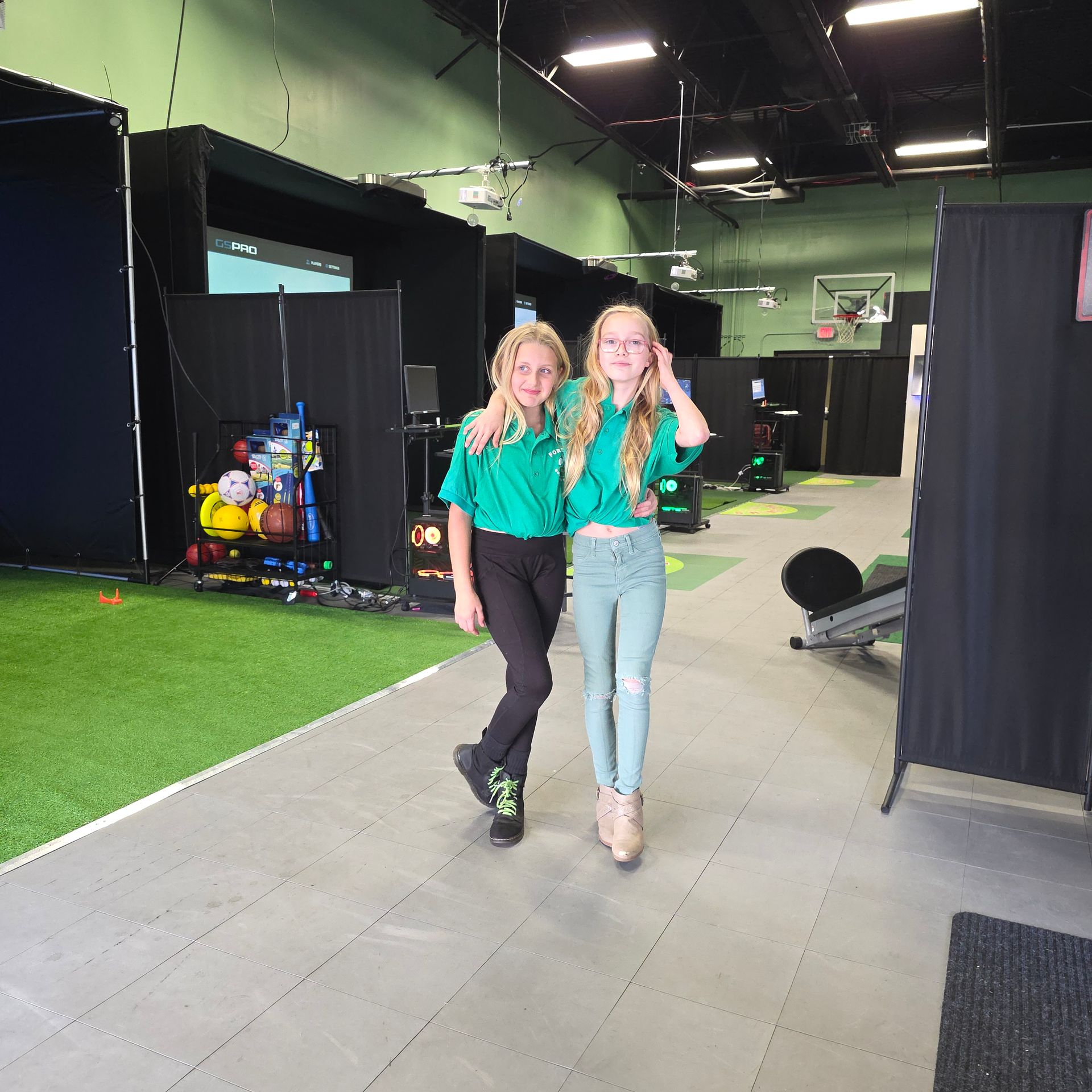 Golf clubs in a row, resting on artificial green turf, leaning against a dark wall.