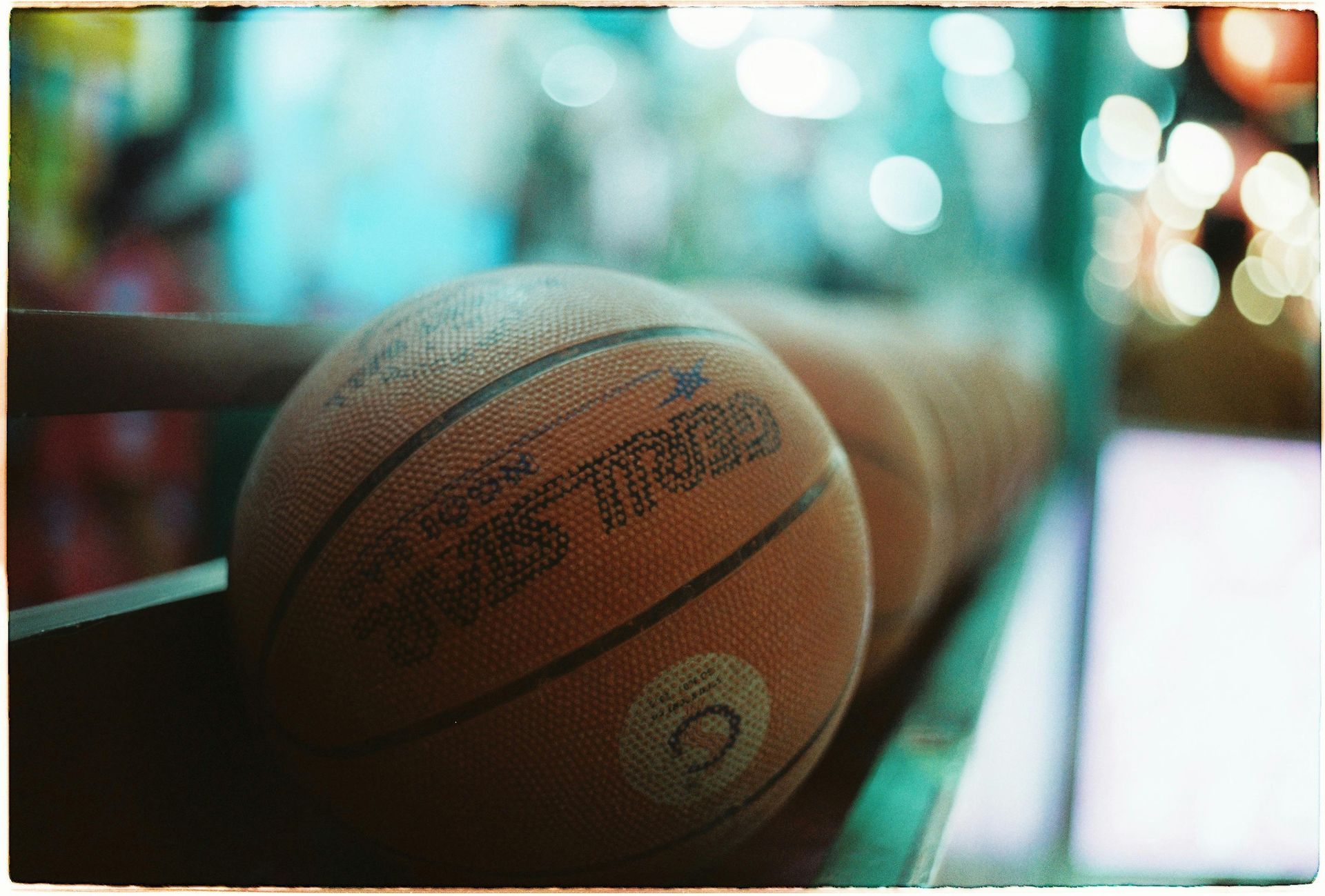 Basketballs lined up on a shelf, lit by soft, blurred background lights.