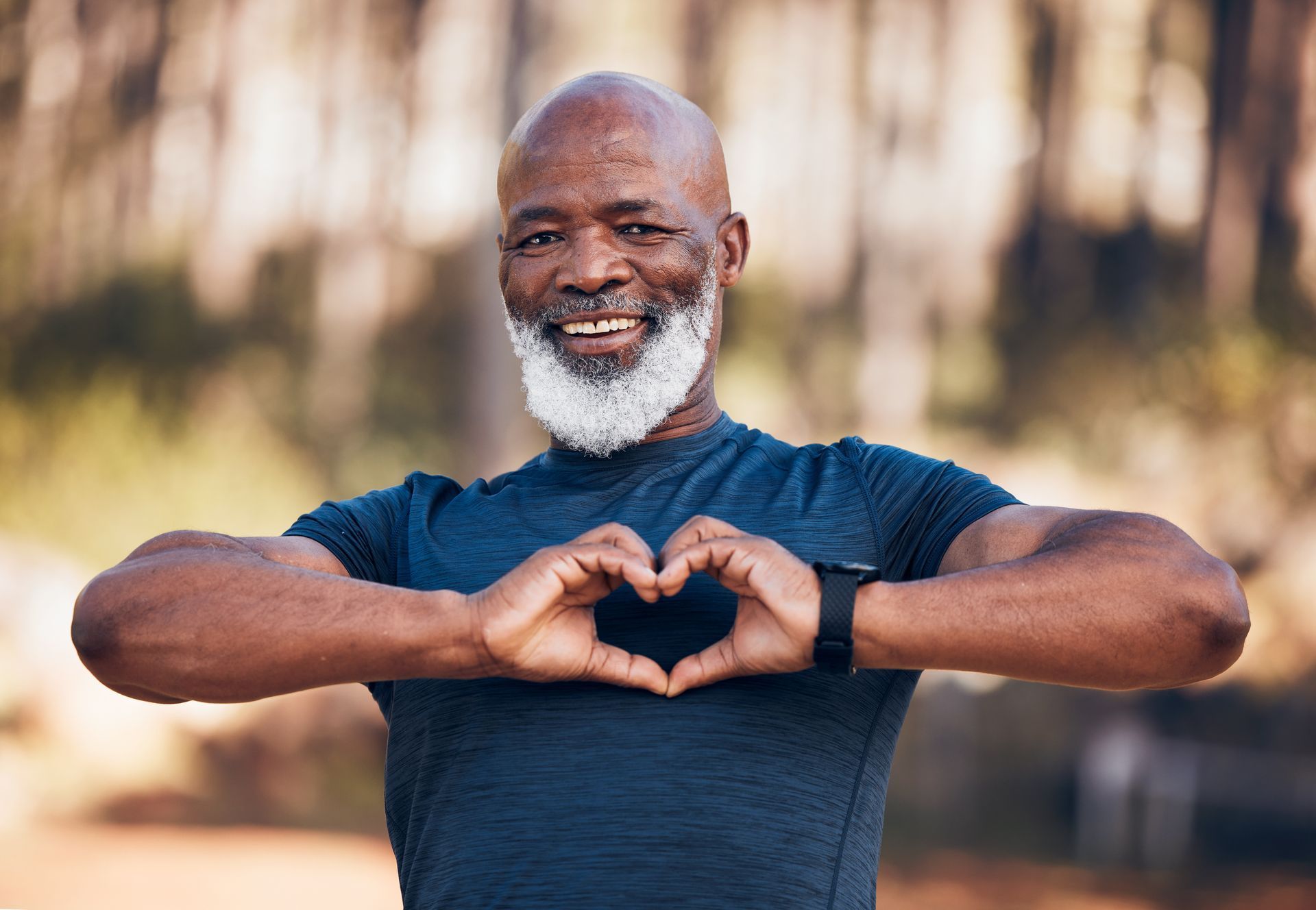 Smiling man in a blue shirt making a heart shape with his hands outdoors