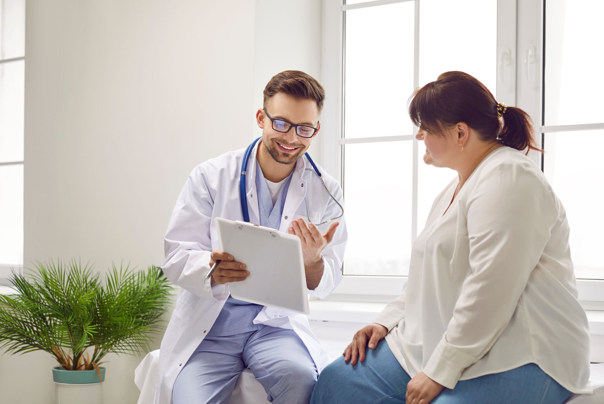 Doctor talking with patient in a bright clinic, holding a clipboard and smiling.