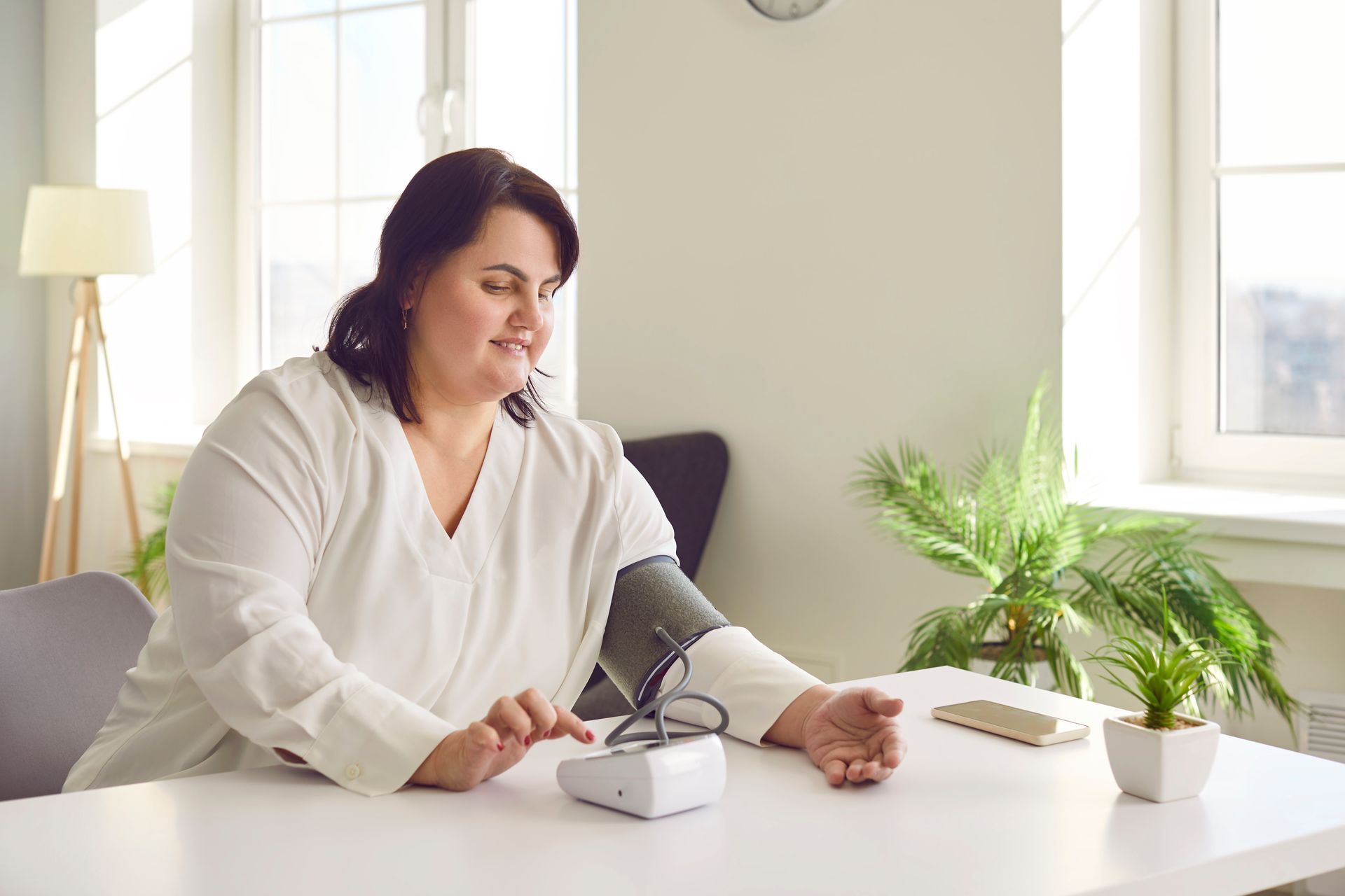 Woman sitting at a desk using a tablet beside a small potted plant in a bright room