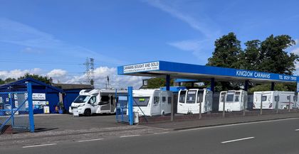 A line of white recreational vehicles parked under a blue-roofed service canopy against a clear blue sky.