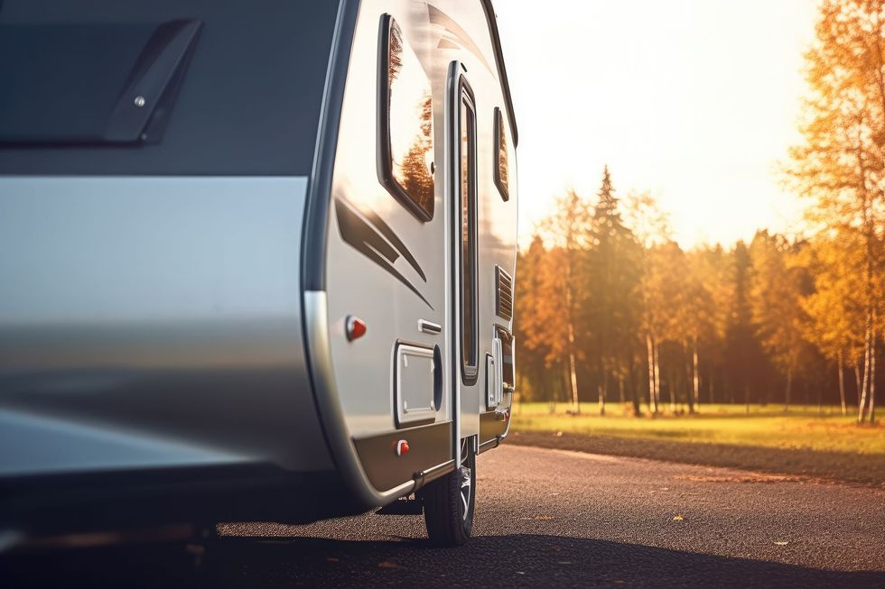 A modern travel trailer parked on a gravel path during sunset with trees in the background.