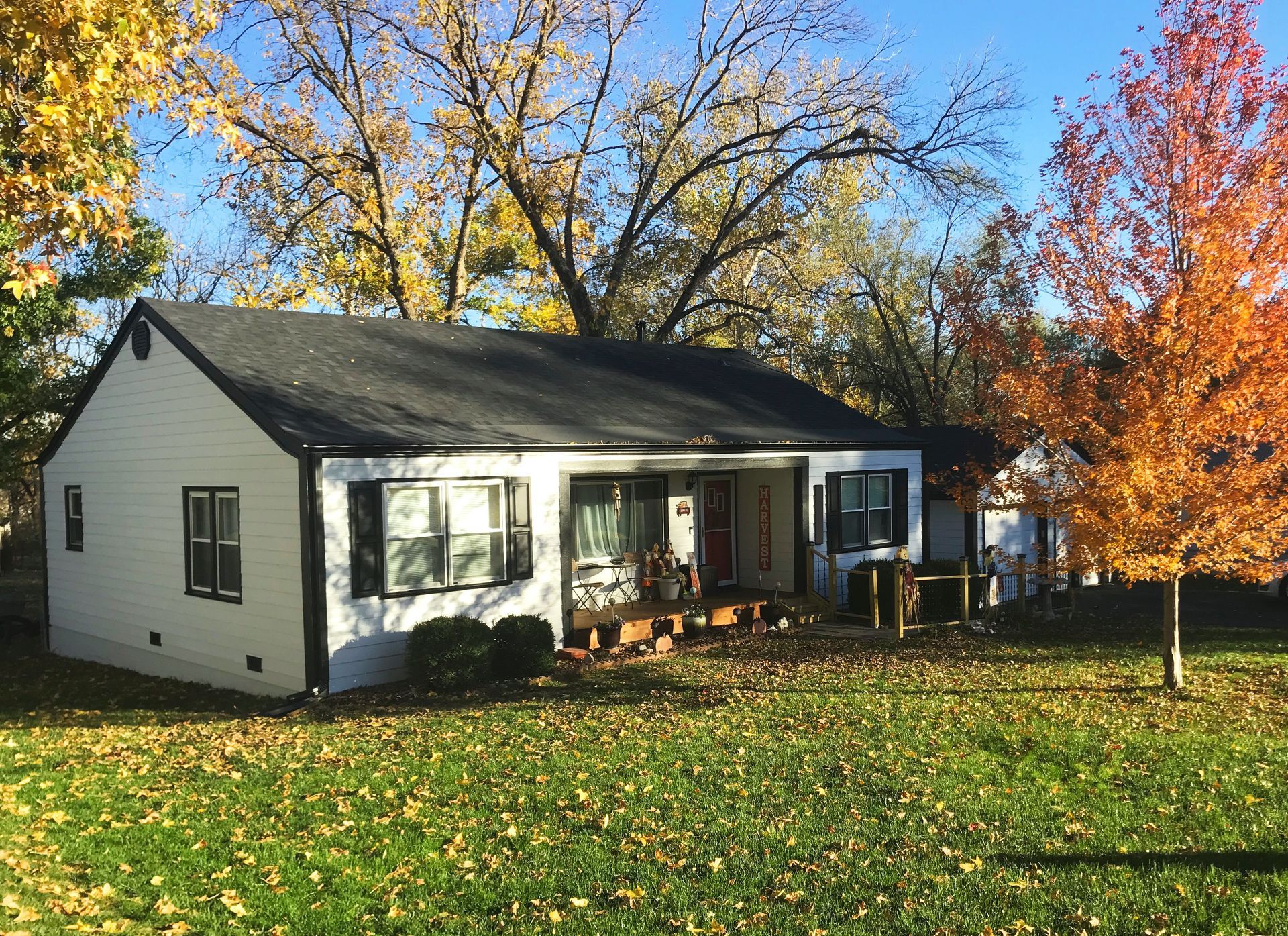 A white house with a black roof is surrounded by trees and leaves.