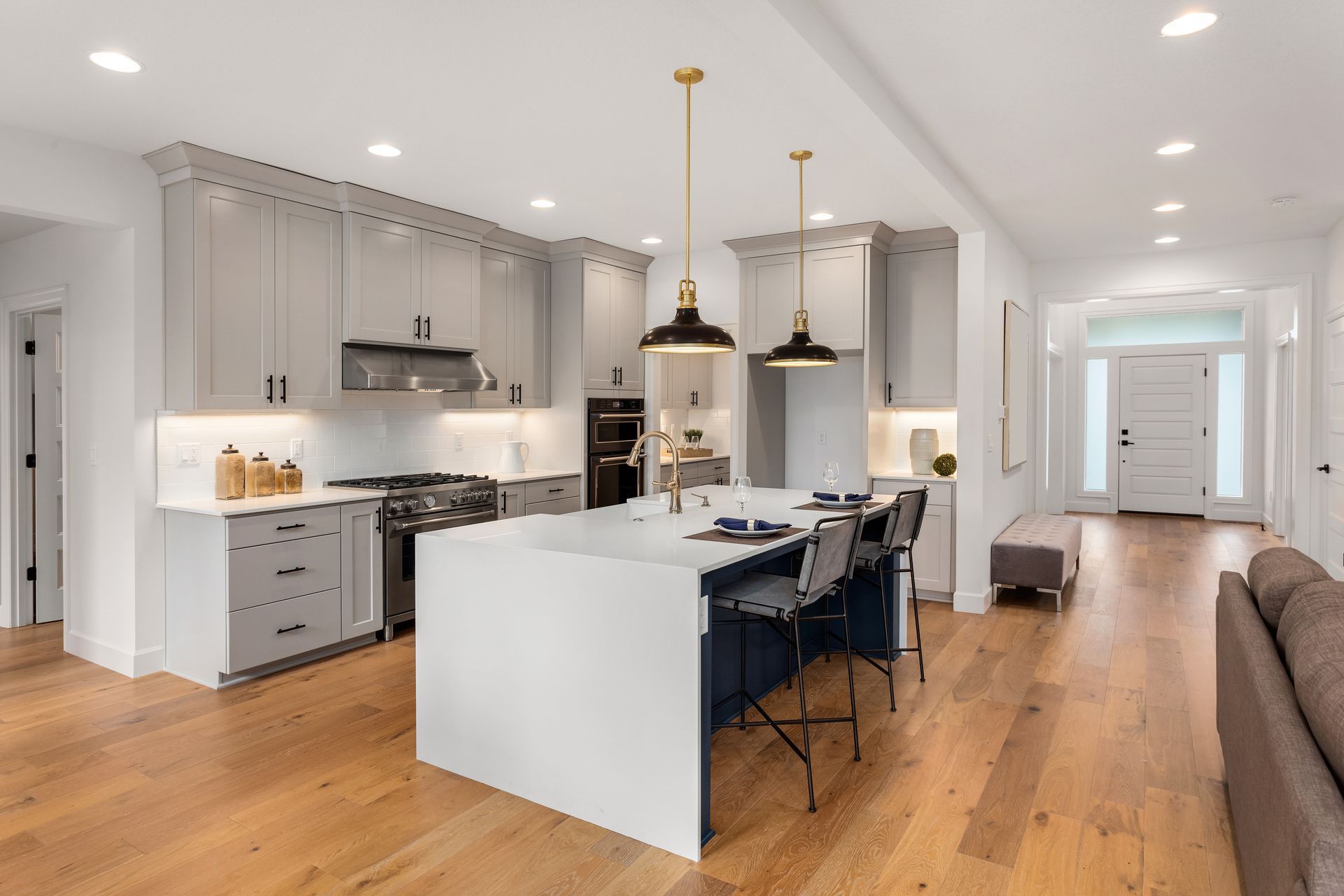 Modern kitchen with gray cabinets, white island, and wooden floors.