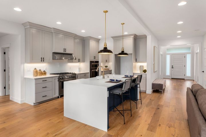 Modern kitchen with gray cabinets, white island, and wooden floors.