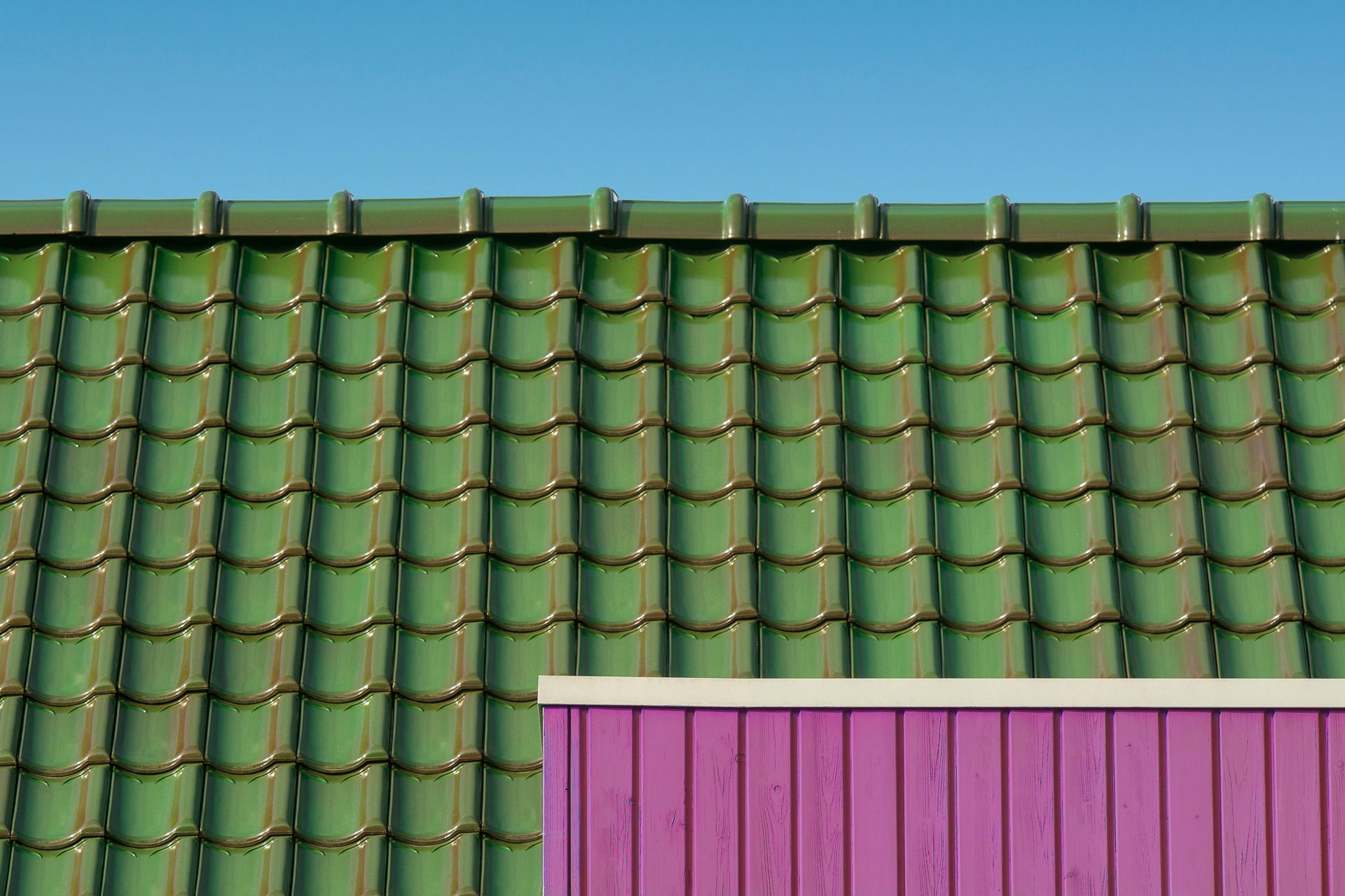 Green tiled roof with a purple wall against a bright blue sky.