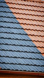 Diagonal view of a roof with two sections: rust-colored tiles and gray tiles.