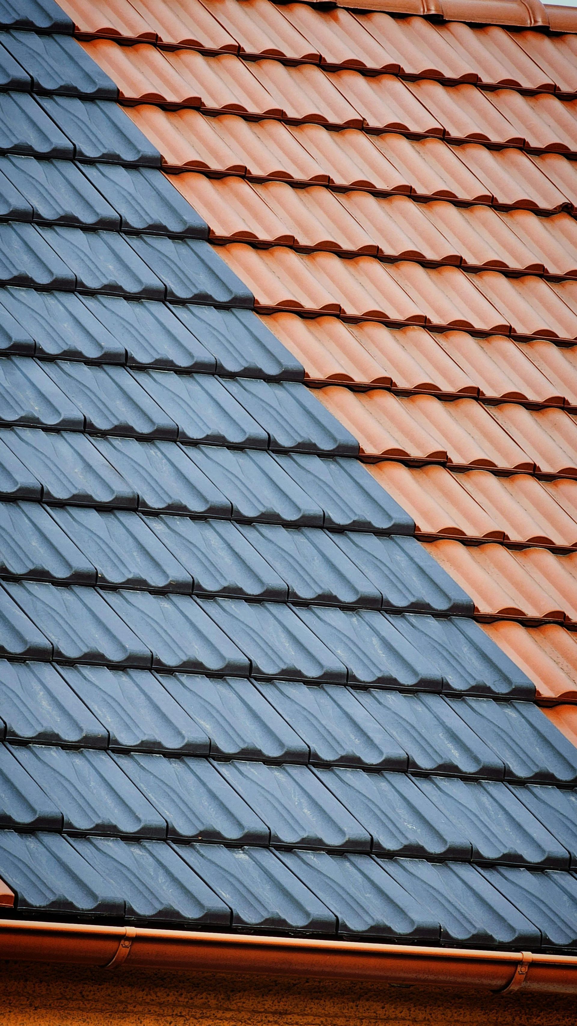 Diagonal view of a roof with two sections: rust-colored tiles and gray tiles.