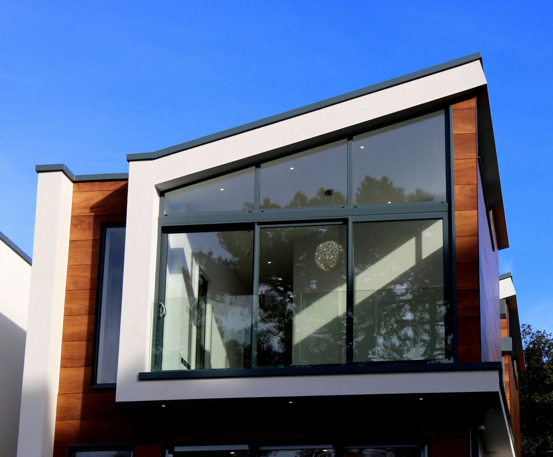 Modern house with a large glass window, wood paneling, and a bright blue sky.