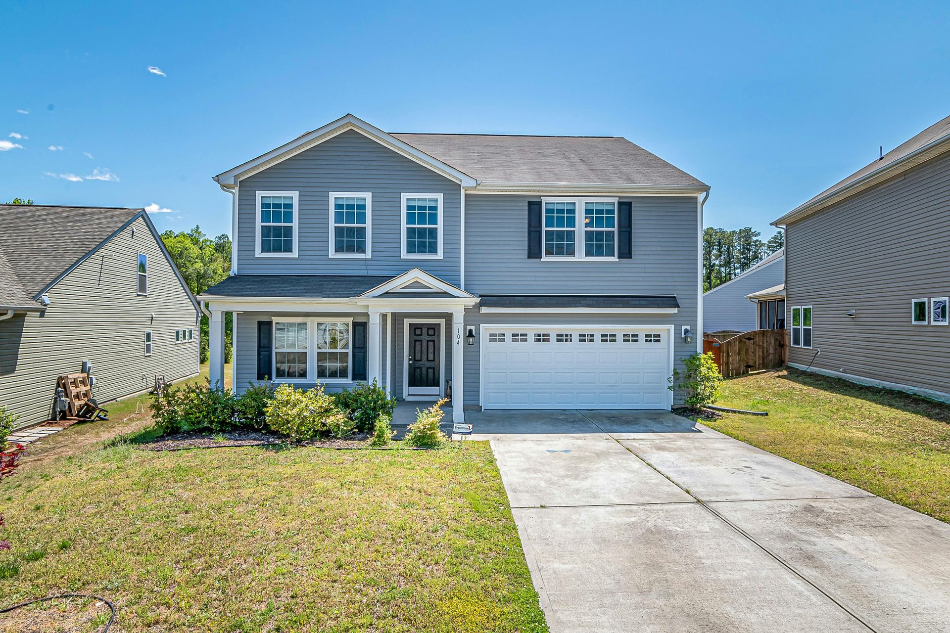 Two-story blue house with white garage door and black shutters; a driveway leads to the front door.