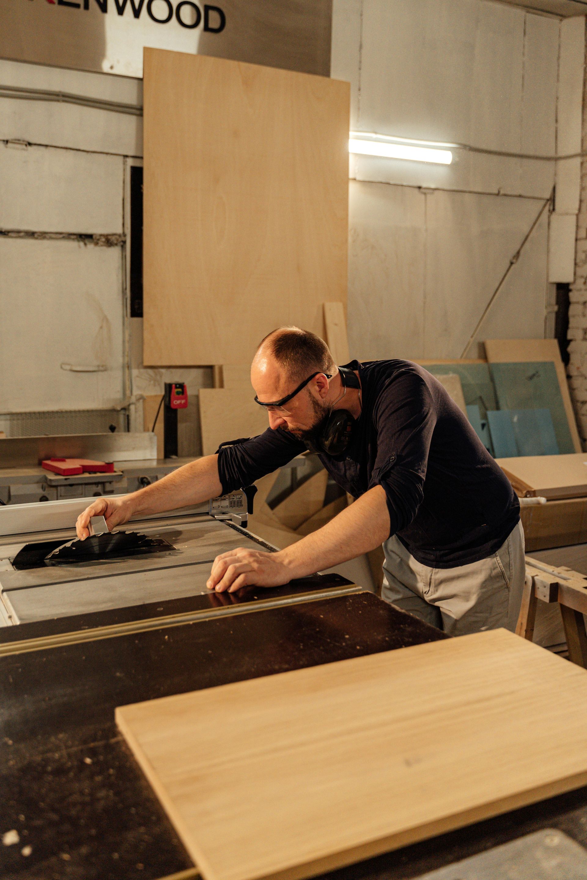 A person wearing safety glasses and ear protection operating a table saw in a workshop.