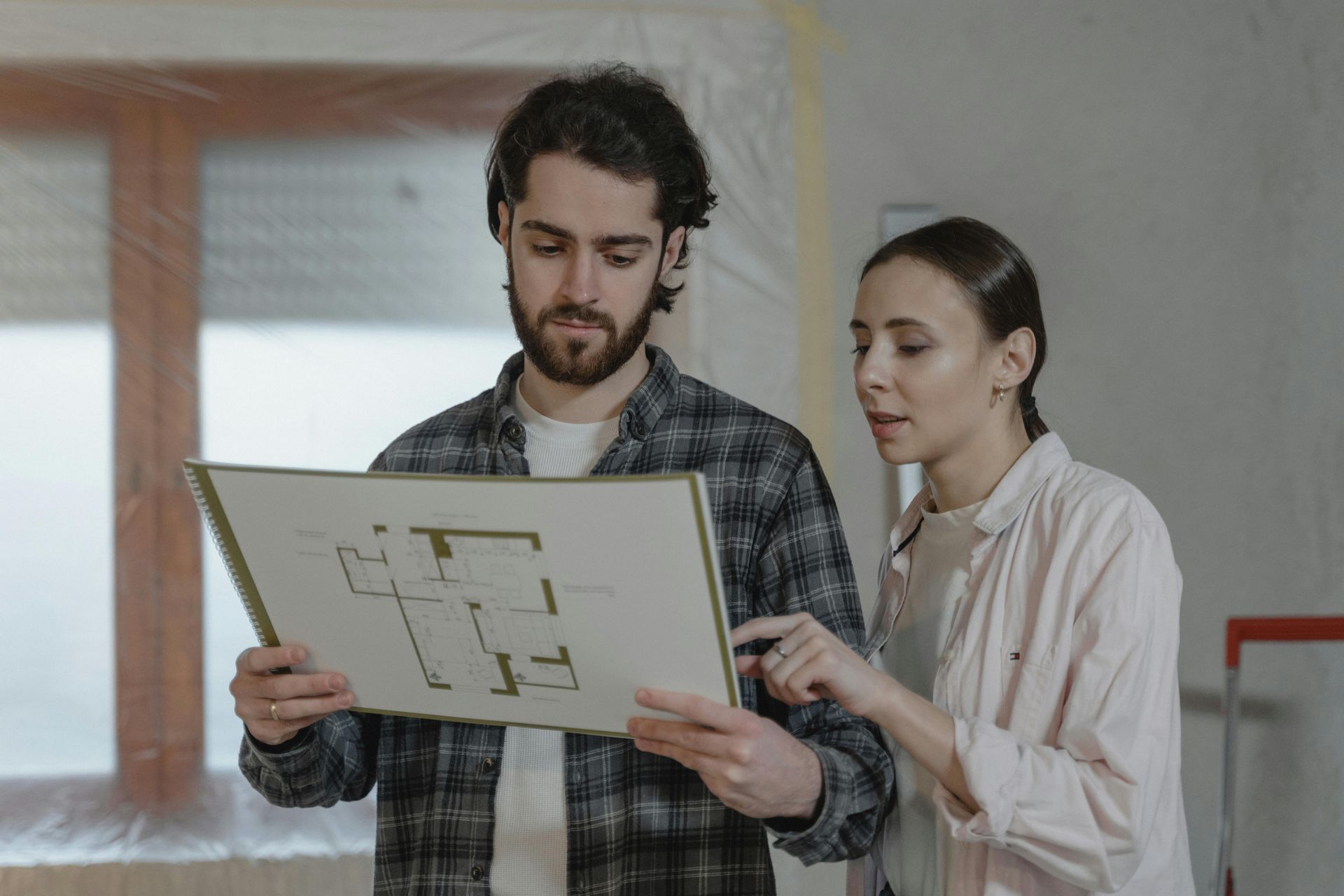 Couple examining a blueprint in a room under renovation. Woman points, man holds the plan.