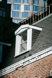 Dormer window on brick building.  A tall modern building rises in the background.