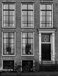 Brick building facade with tall windows, black door, and bicycles parked in front.