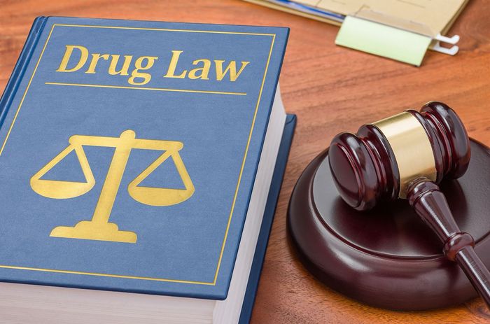 Drug law book with scales icon beside a judge’s gavel on a desk Drug law book with scales icon beside a judge’s gavel on a desk
