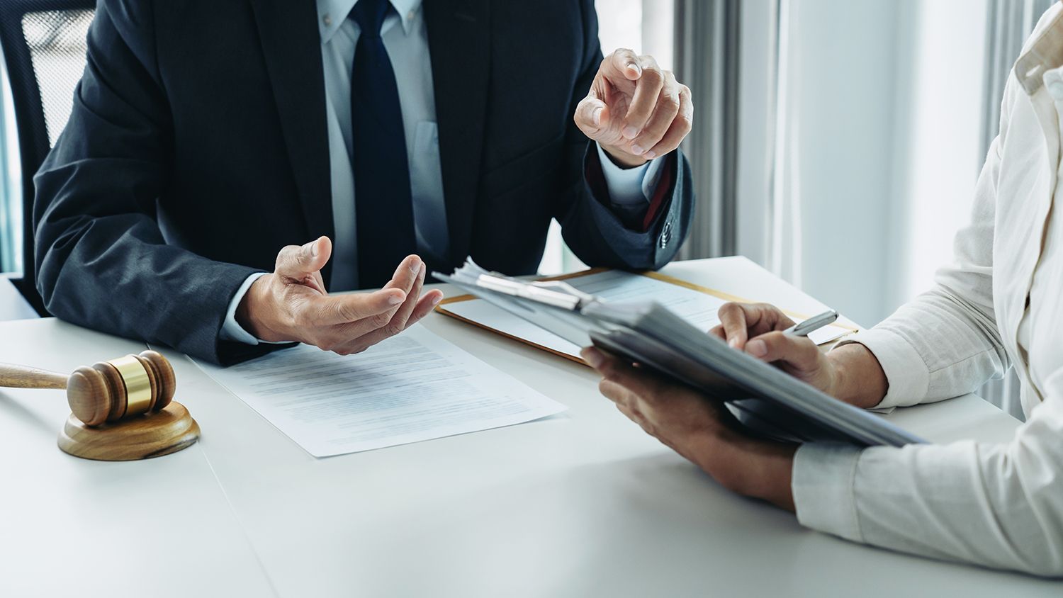 Two people discussing a contract at a desk, with a gavel and documents in a bright office. Two people discussing a contract at a desk, with a gavel and documents in a bright office.