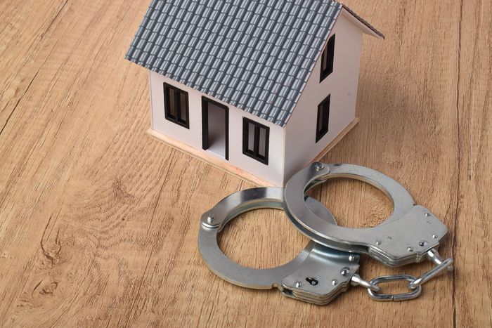Two metal handcuffs beside a small model house on a wooden surface Two metal handcuffs beside a small model house on a wooden surface