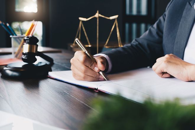 Lawyer writing at desk with gavel and scales of justice in the background Lawyer writing at desk with gavel and scales of justice in the background