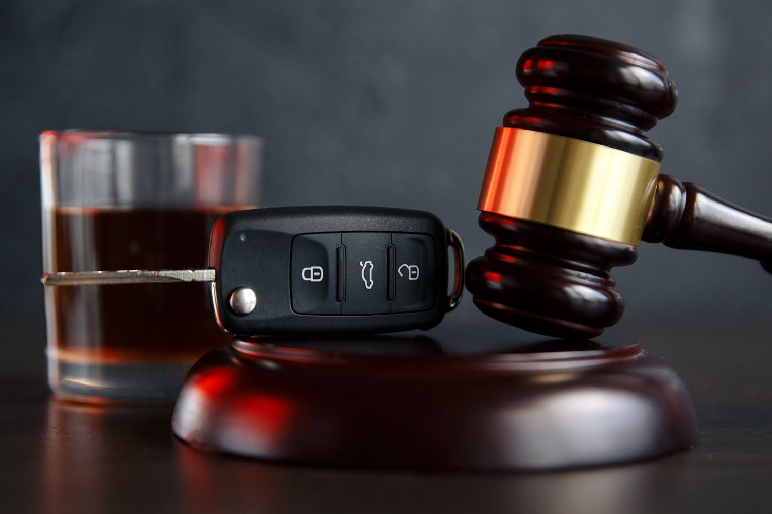 Car key fob beside a judge’s gavel and glass of whiskey on a dark table, suggesting a DUI arrest. Car key fob beside a judge’s gavel and glass of whiskey on a dark table, suggesting a DUI arrest.