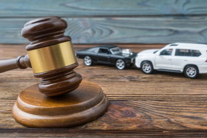 Gavel on wooden desk with two parked cars in the background, suggesting a legal auto case Gavel on wooden desk with two parked cars in the background, suggesting a legal auto case