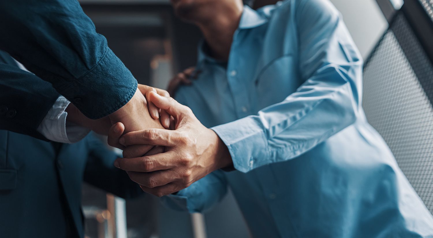 Two people in blue shirts shaking hands in a professional setting Two people in blue shirts shaking hands in a professional setting