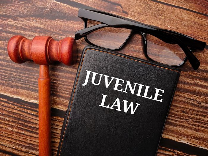 Juvenile law book beside a gavel and eyeglasses on a wooden desk Juvenile law book beside a gavel and eyeglasses on a wooden desk