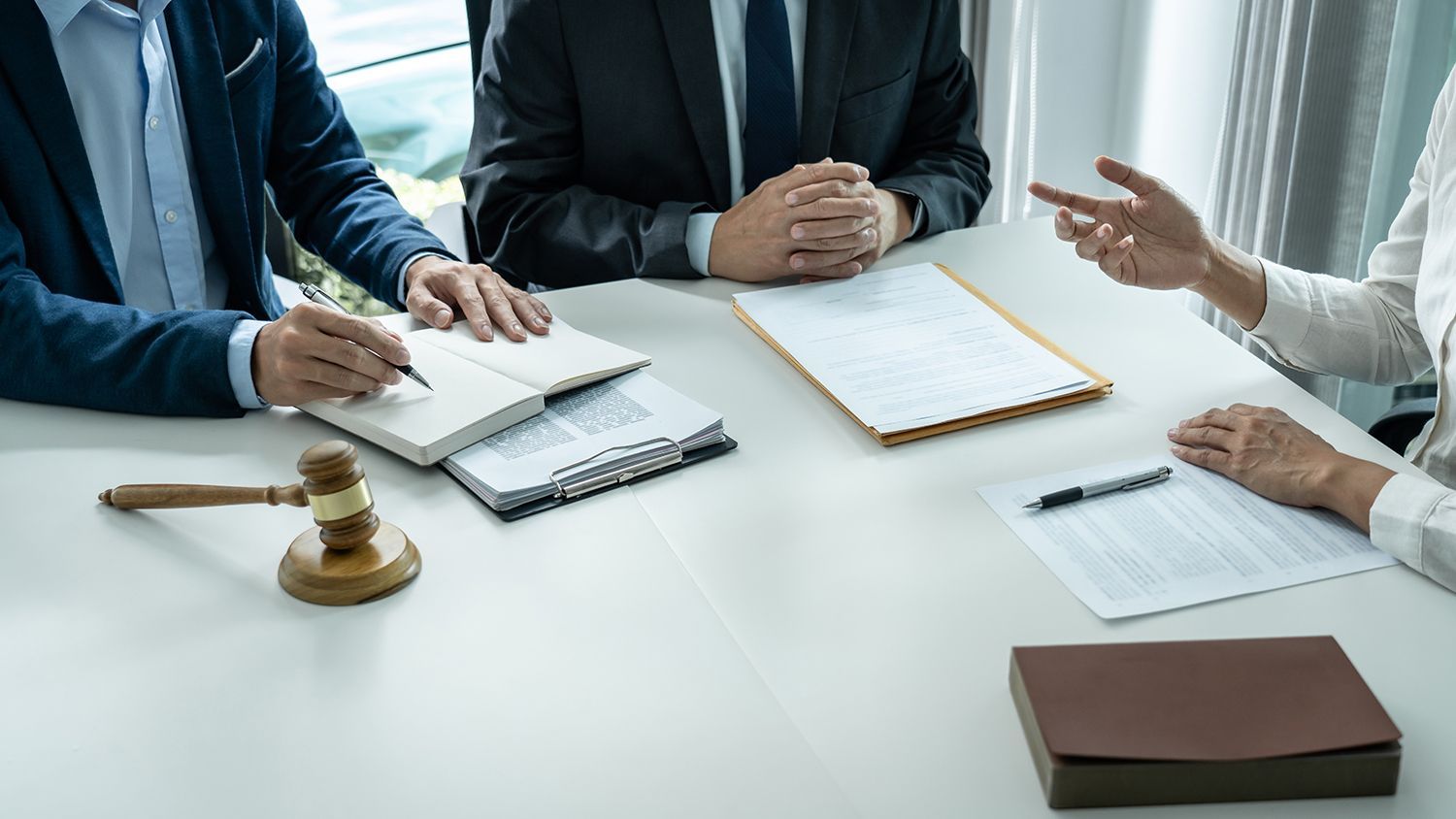 Business meeting with people signing documents at a white conference table, with a gavel and folder nearby Business meeting with people signing documents at a white conference table, with a gavel and folder nearby