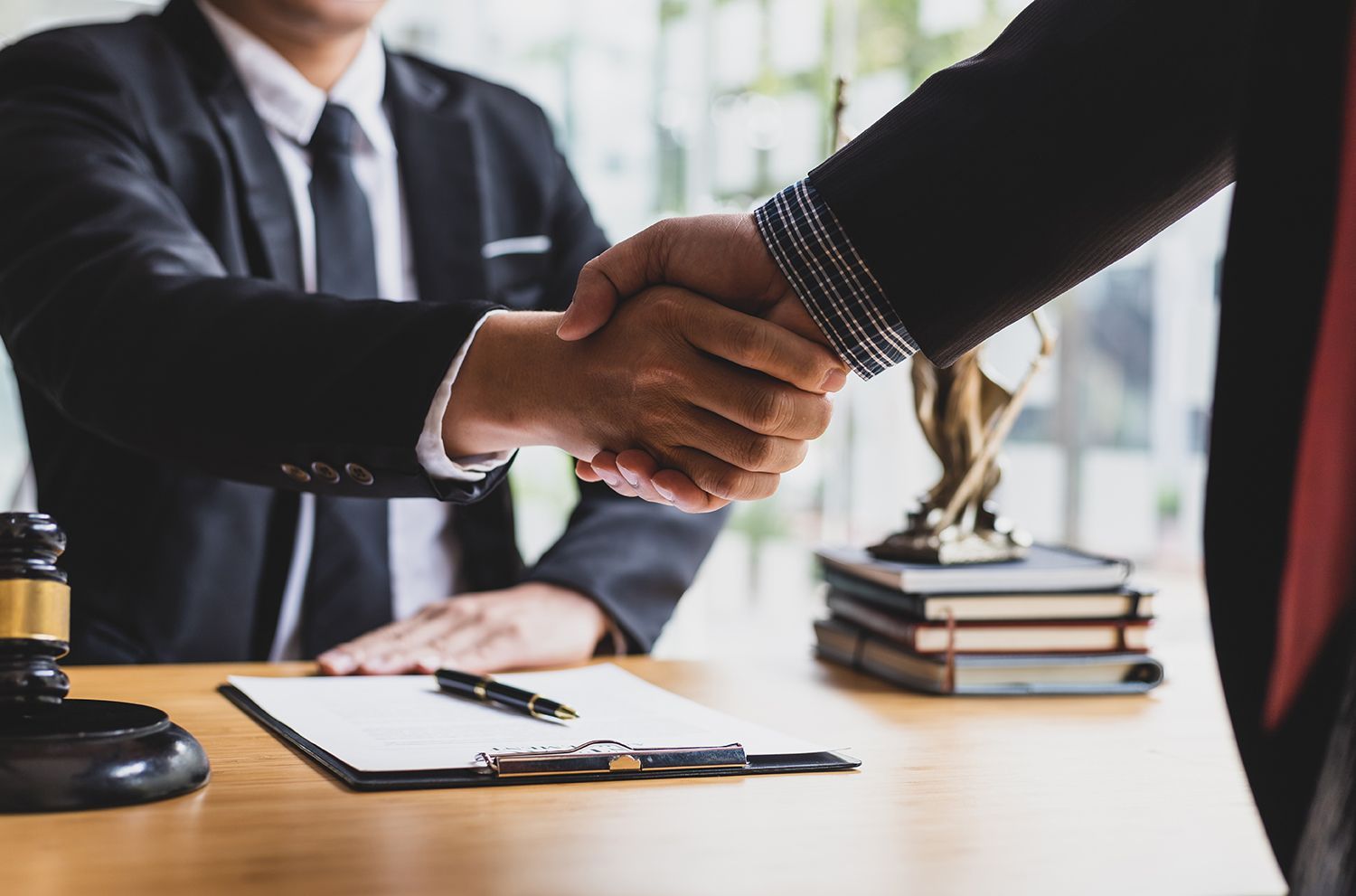 Business people shaking hands across a desk with documents and pens in a bright office Business people shaking hands across a desk with documents and pens in a bright office