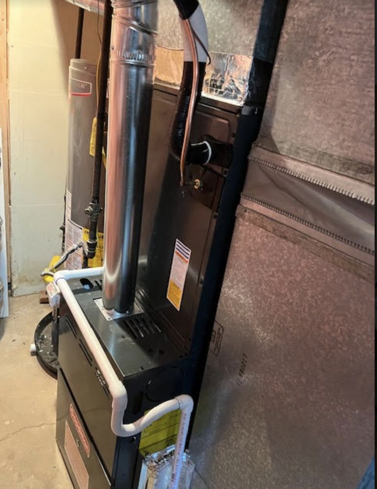 Furnace in a basement; gray metallic walls, silver exhaust pipe, and black control panel.