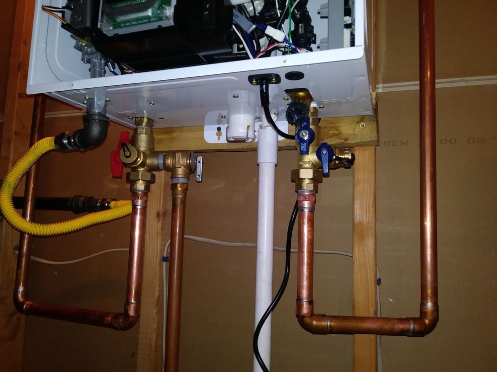 Copper pipes and valves connected to a white wall-mounted boiler. Black gas line, blue & red valve handles.