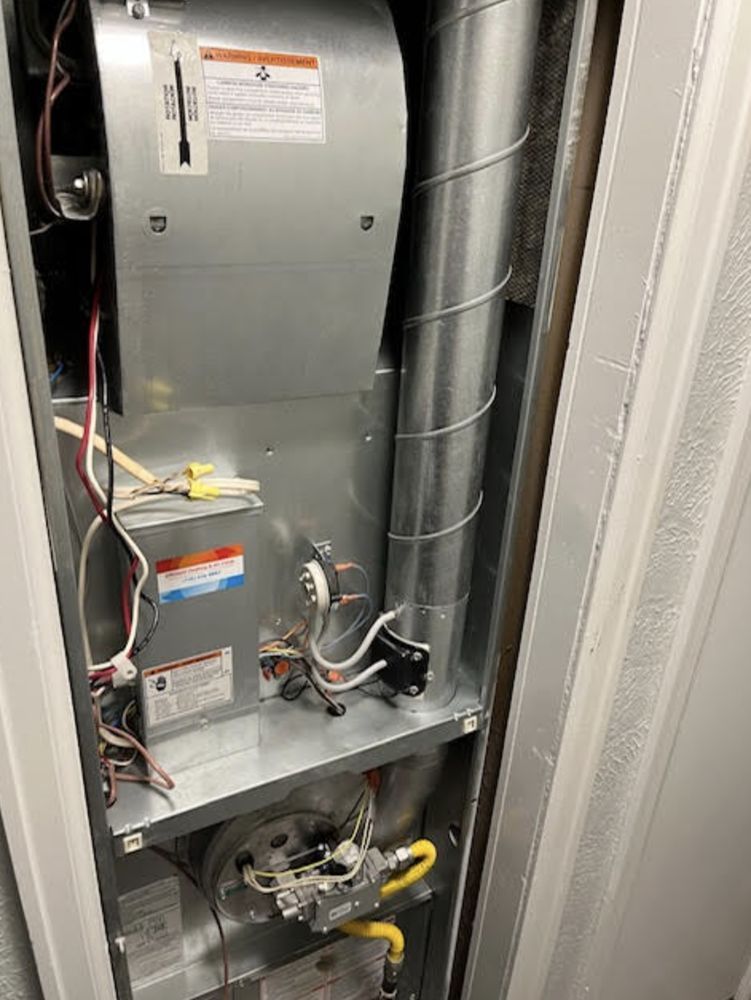 Furnace unit in a closet with metal ductwork, wires, and safety labels.