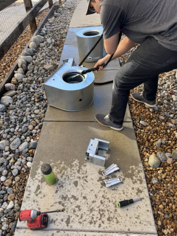Person cleaning metal components outdoors with spray and tools.