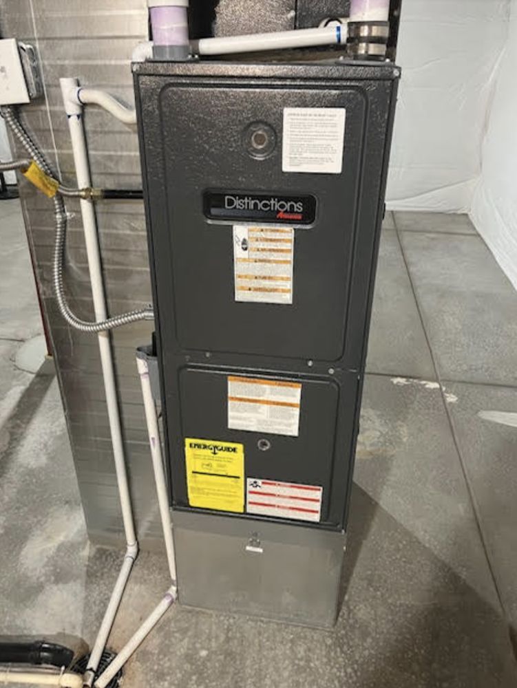 A dark grey furnace with a metal filter in a basement setting.