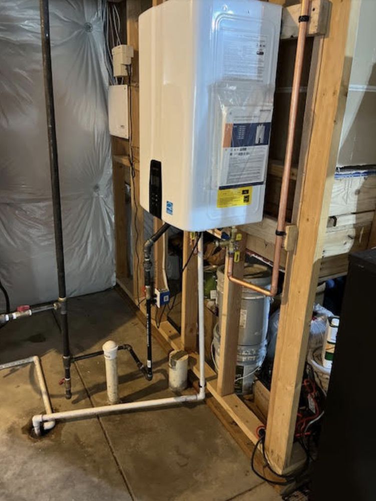 Tankless water heater installation with copper pipes and white PVC in a basement.