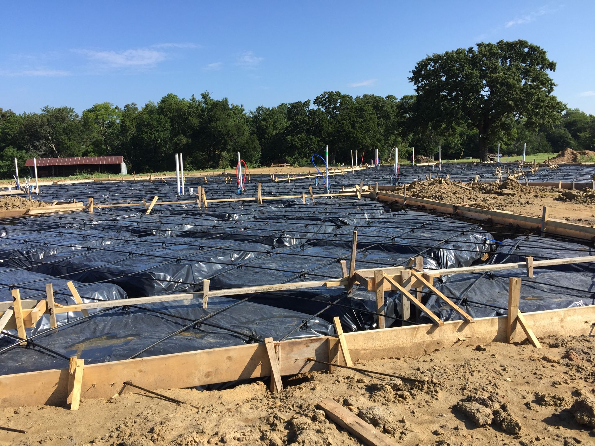 Construction site with wooden forms, rebar, and black plastic sheeting, ready for concrete foundation.