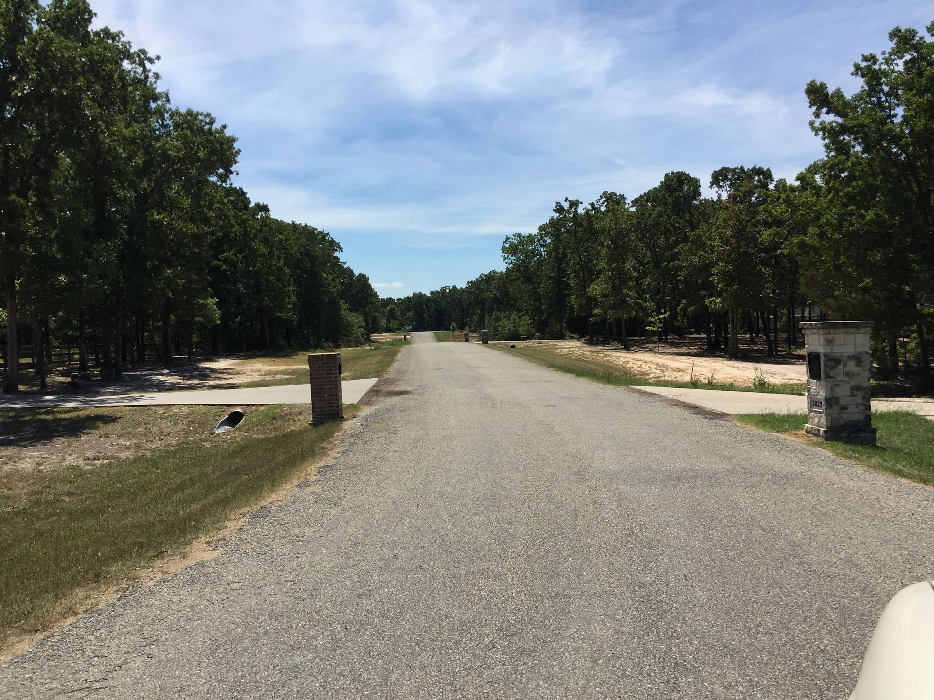 Gravel road lined with trees on either side stretches towards the horizon under a partly cloudy sky.