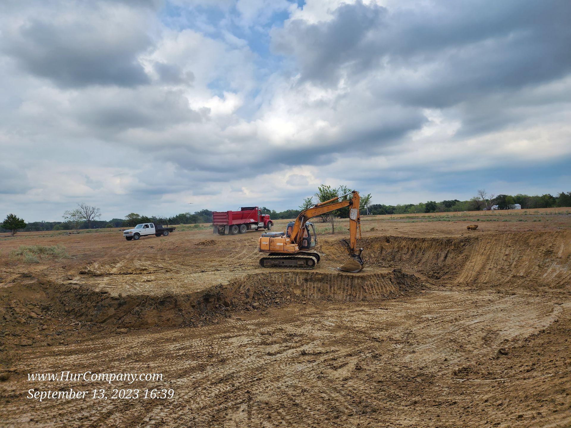 An excavator digs into a muddy field under a cloudy sky.