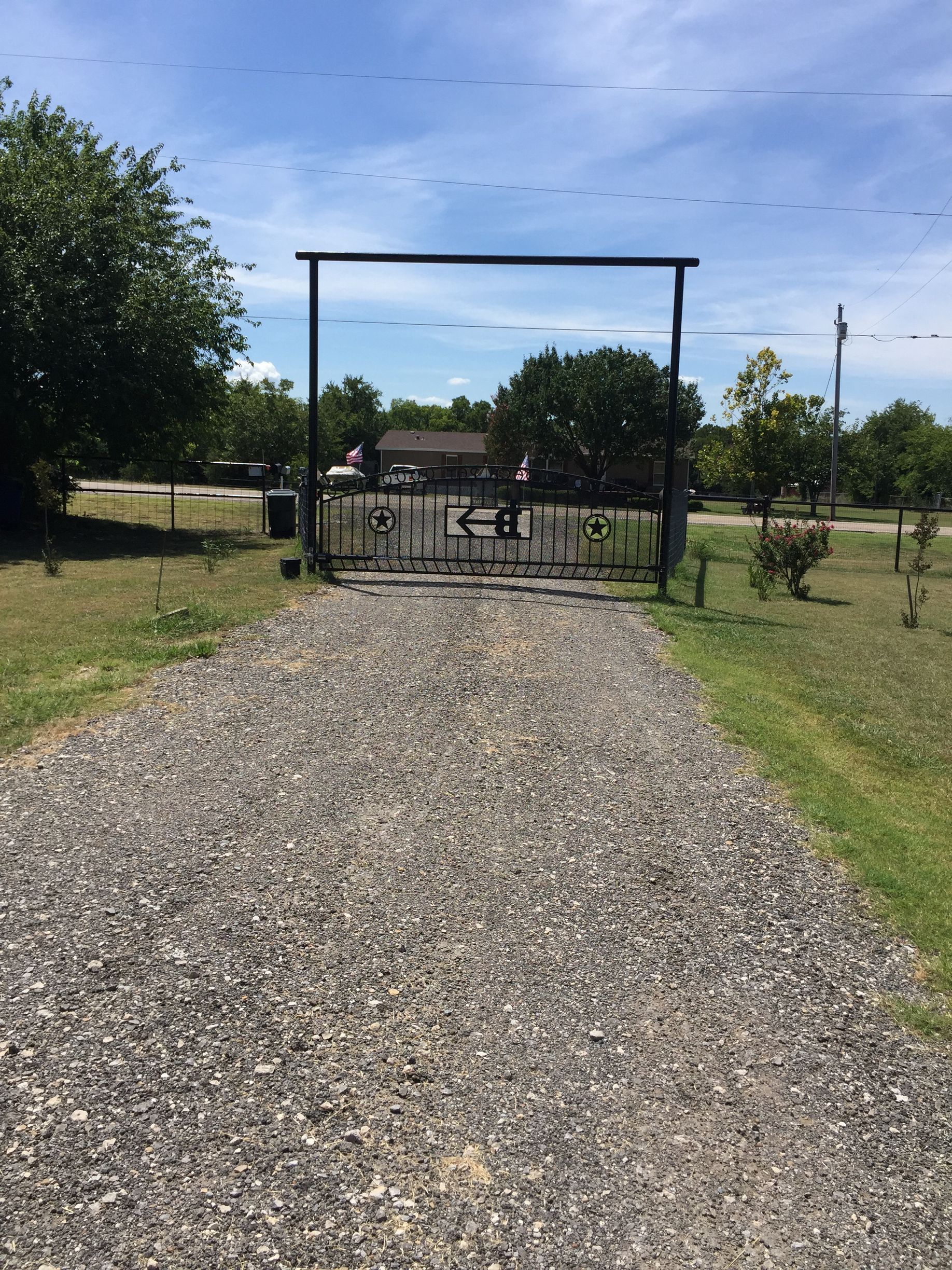 Gravel path leading to a black gate with a person standing inside.