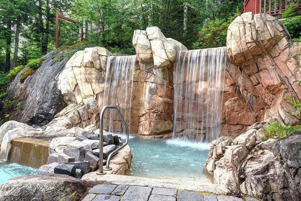 Une cascade est entourée de rochers et d'arbres et il y a une piscine devant elle.