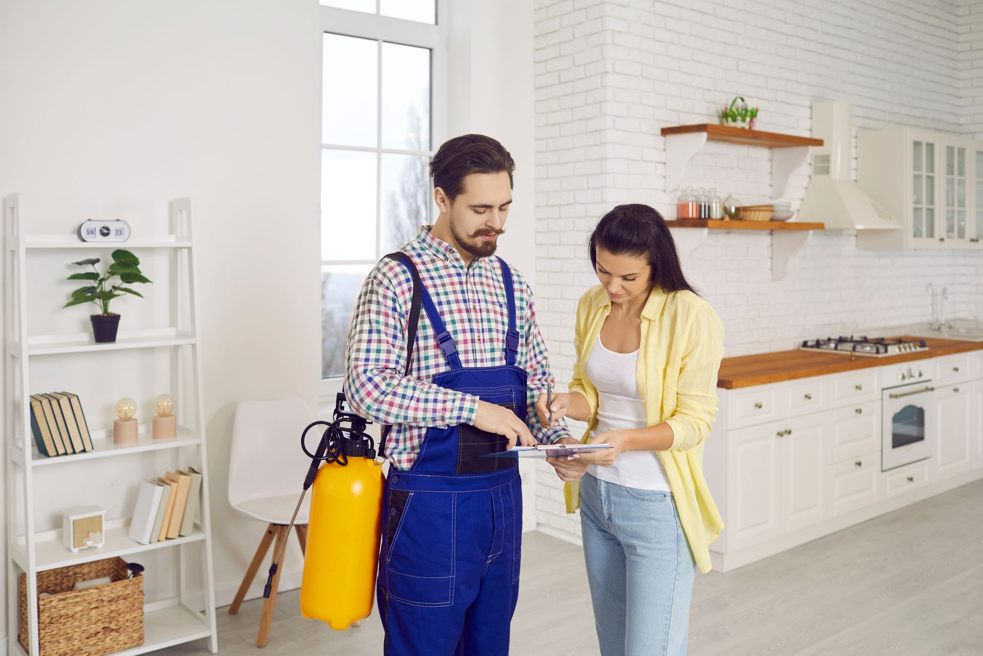 Two people in a bright kitchen using a yellow fire extinguisher near the stove
