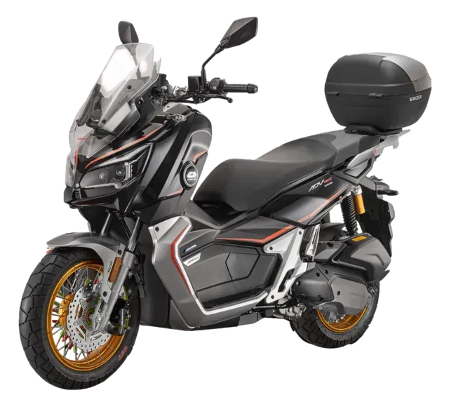 Uno scooter da avventura nero e grigio con ruote a raggi con bordo dorato e vano portaoggetti posteriore su sfondo bianco.