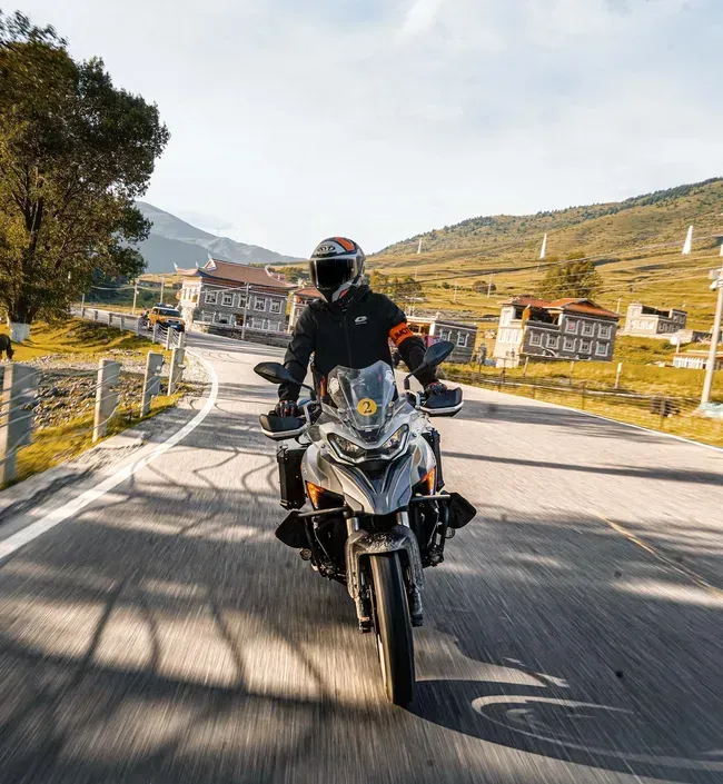 Una persona con il casco in testa percorre in moto una strada asfaltata in un paesaggio montuoso.