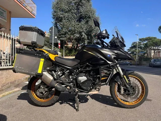 Una moto da avventura nera con cerchi dorati e valigie in alluminio parcheggiata su una strada