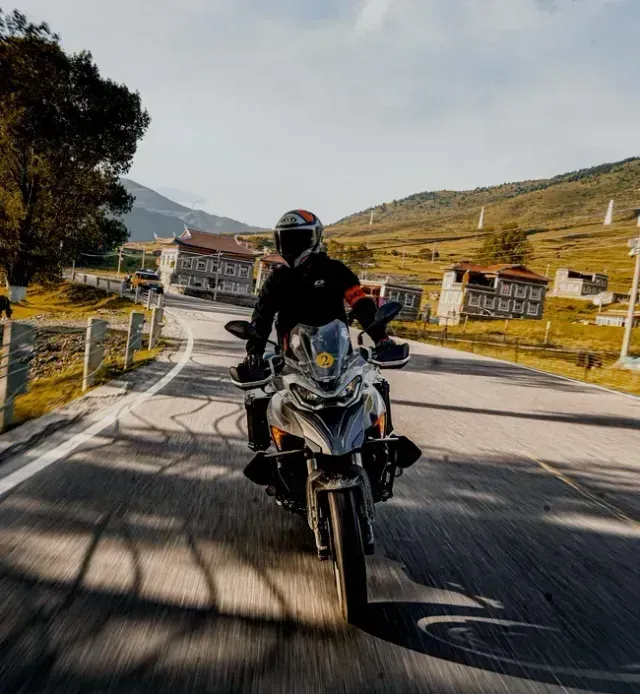 Un motociclista con casco e abbigliamento nero guida una moto da avventura di colore chiaro su una
